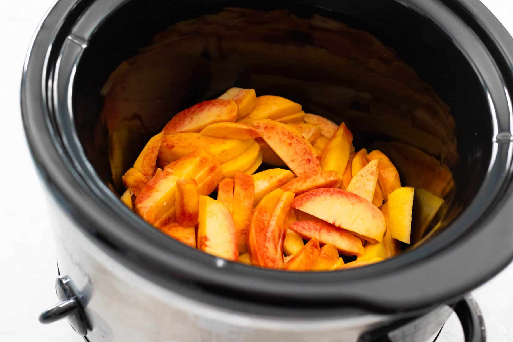 The sliced peaches are in the crockpot bowl.