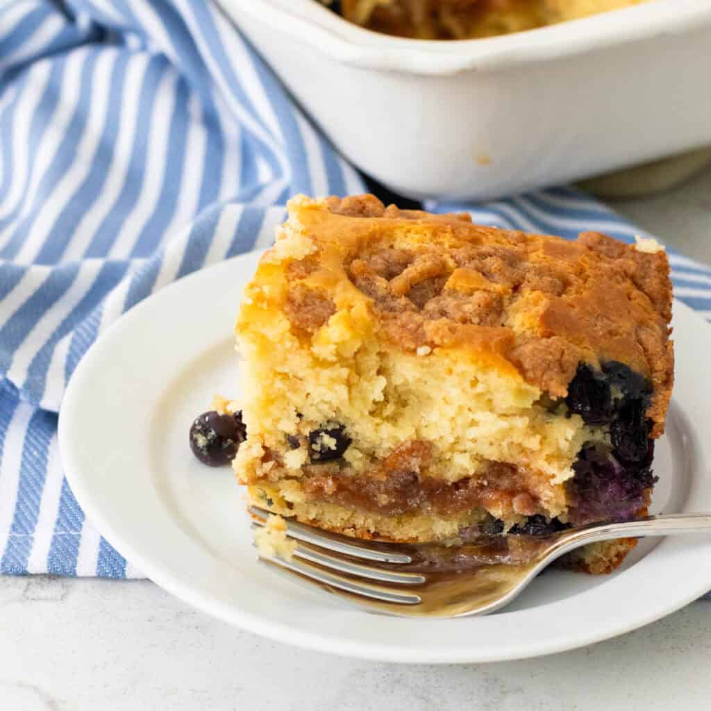 A square of fresh baked coffee cake with a layer of blueberries sits on a plate.