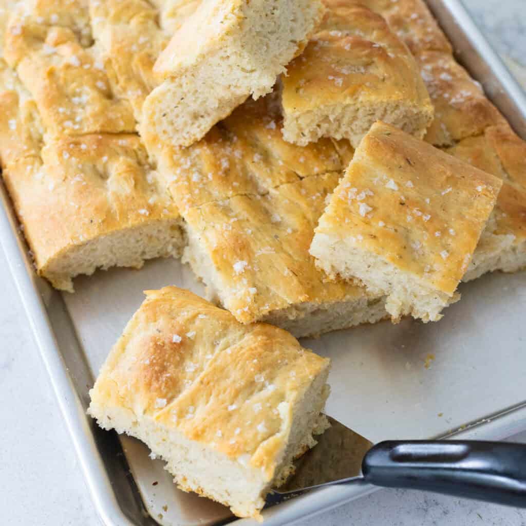 Squares of fresh baked sourdough focaccia are scattered over the baking pan.