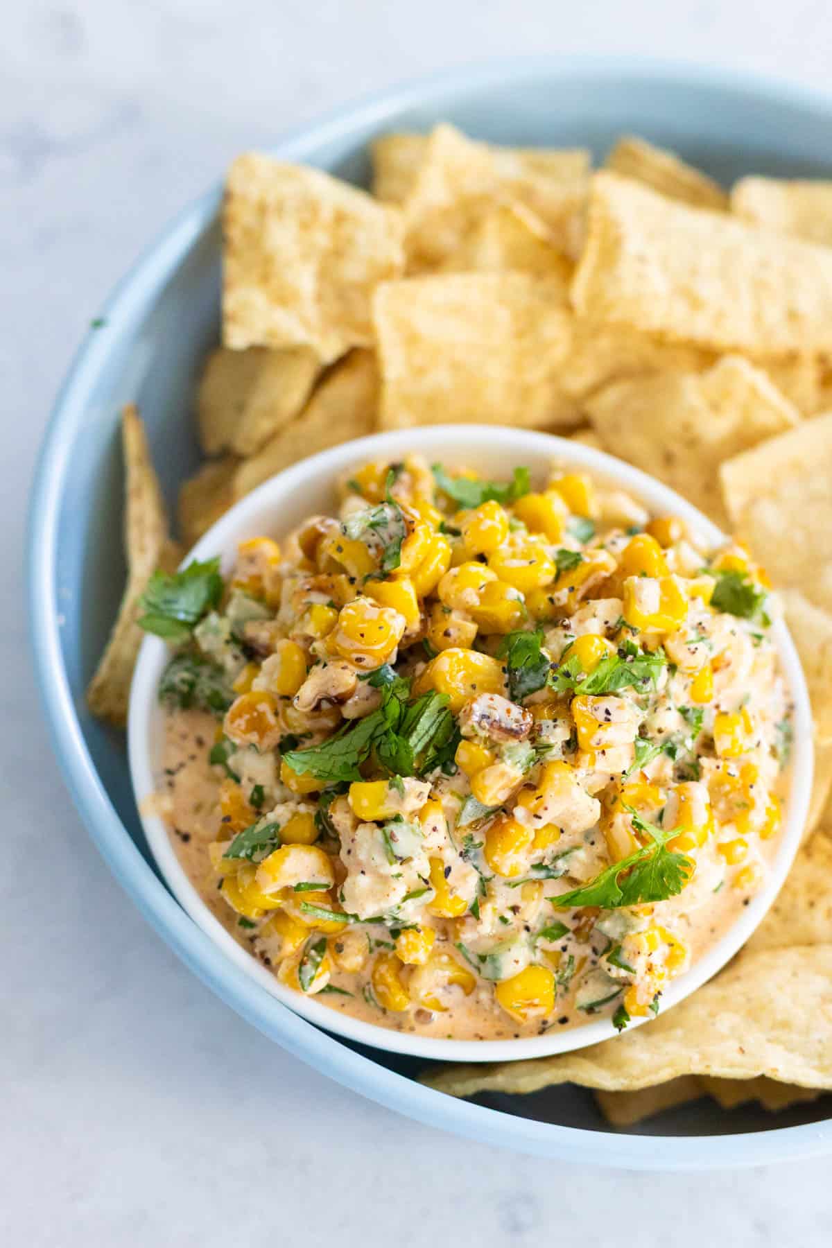 A bowl of tortilla chips has a small bowl of corn dip nestled in the center.
