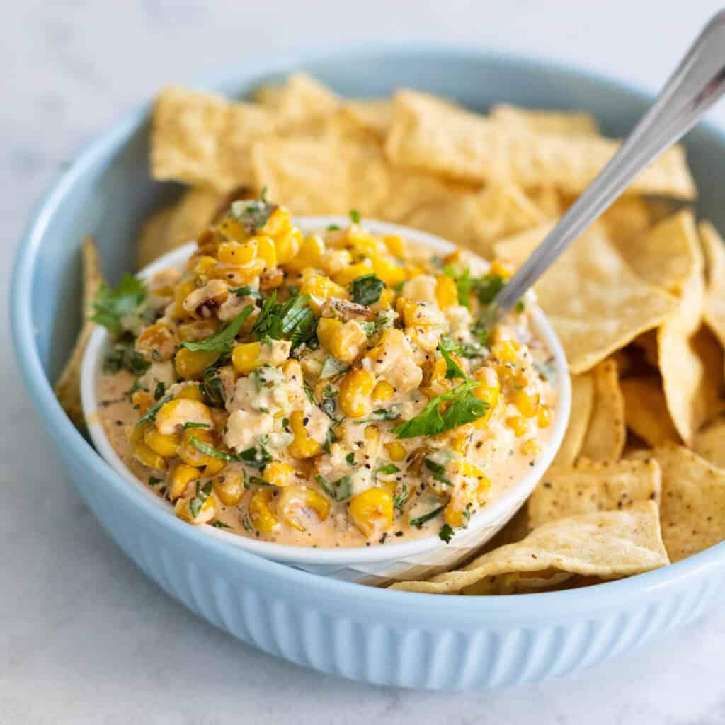 A bowl of tortilla chips has a small bowl of corn dip nestled in the center.