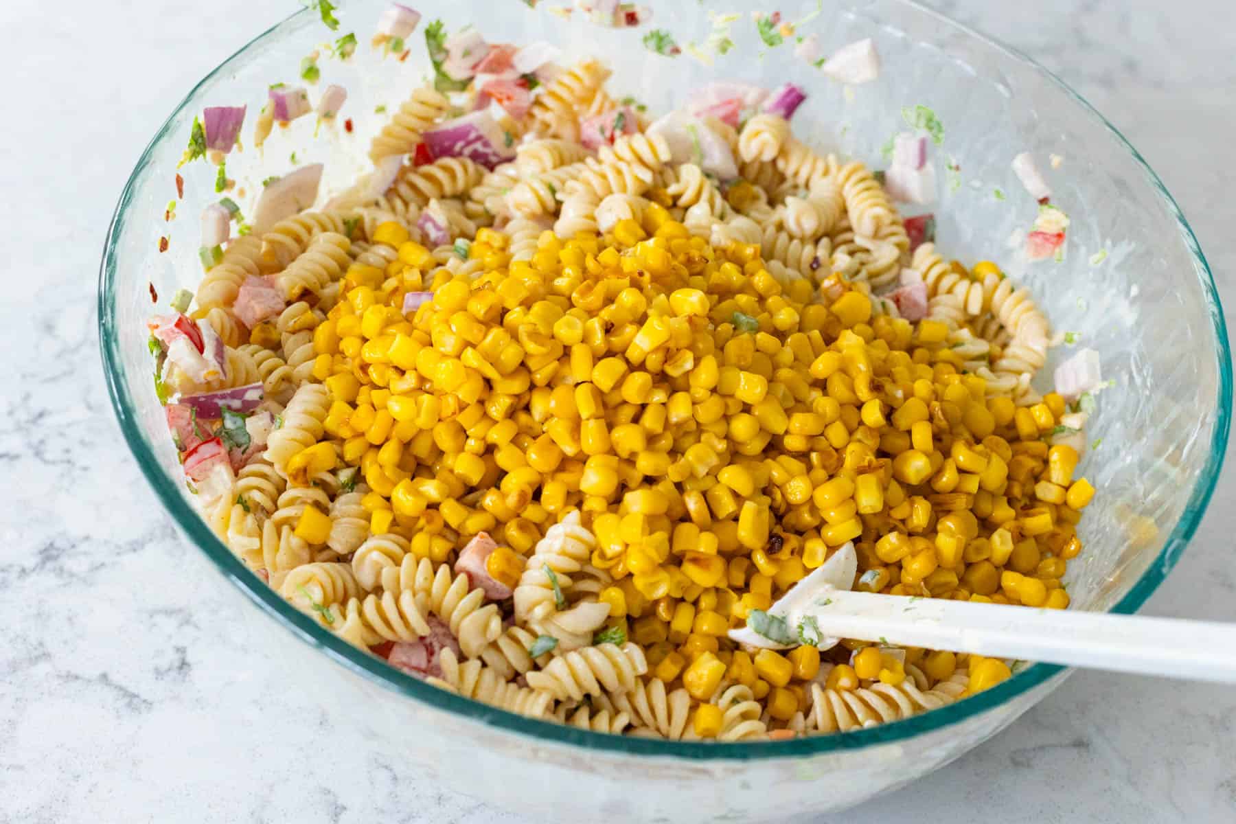 The pasta and sweet corn have been added to the mixing bowl.