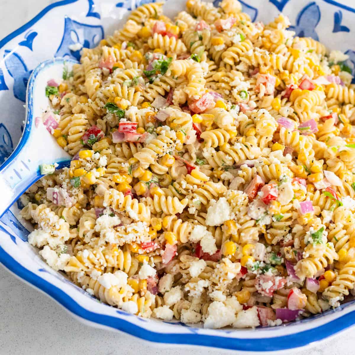 A blue and white bowl is filled with a creamy sweet corn pasta salad.