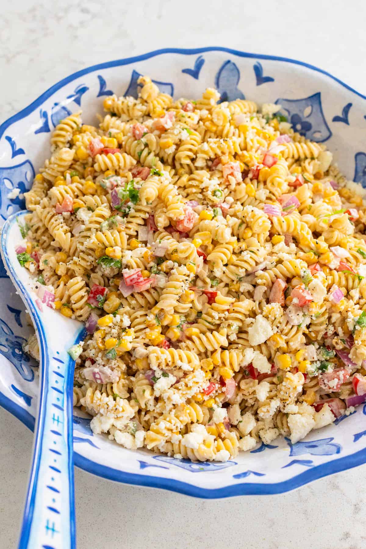The pasta salad is served in a large bowl with a serving spoon on the side.
