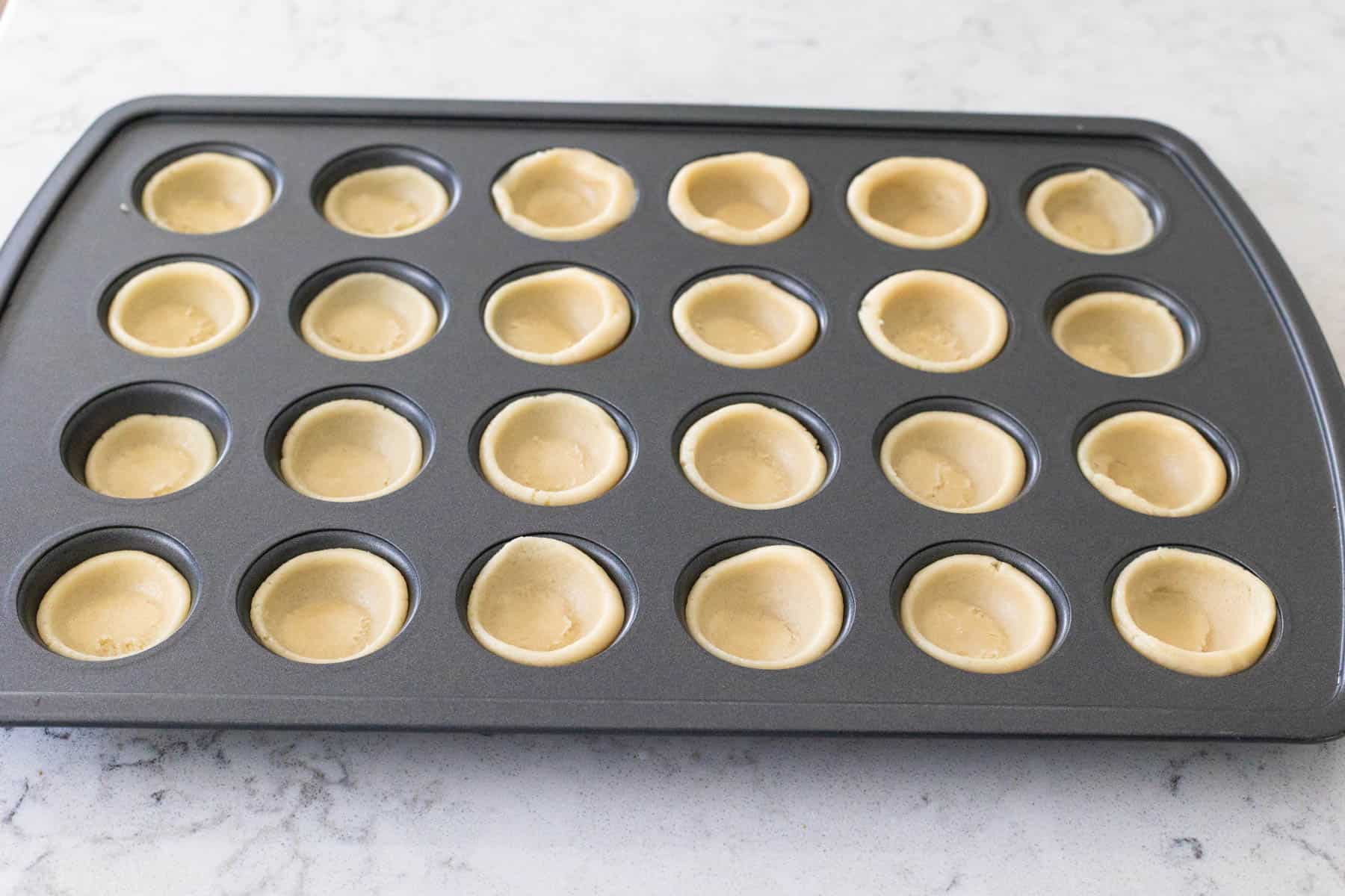 Mini muffin tin filled with evenly pressed sugar cookie dough cups, shaped and ready to go into the oven.