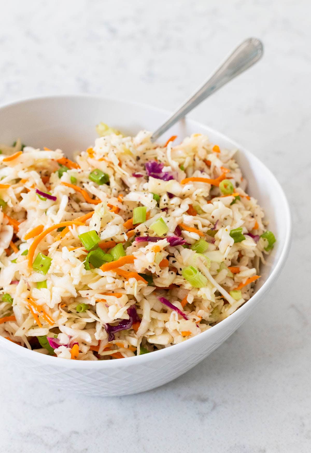 A vinegar-based slaw is in a white bowl with a spoon ready to scoop it.