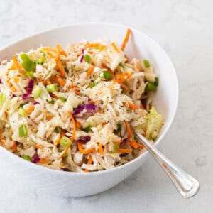 A vinegar-based slaw is in a white bowl with a spoon ready to scoop it.