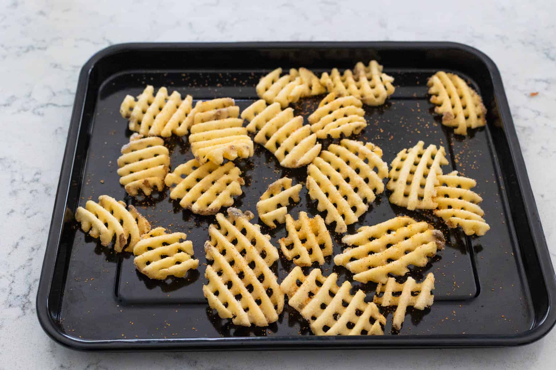 Waffle-cut fries seasoned and baked on a black baking tray.