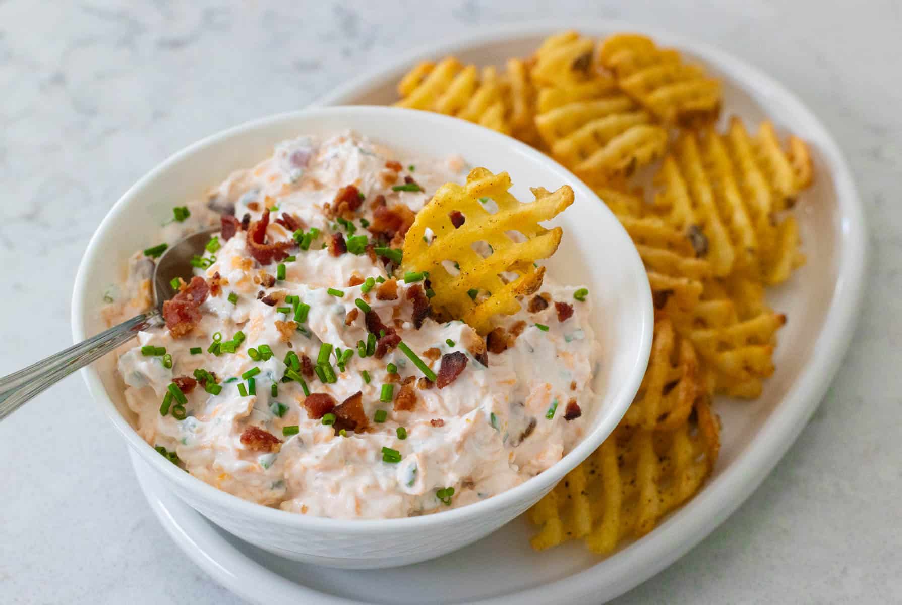 Creamy baked potato dip topped with bacon and chives, served with waffle fries.