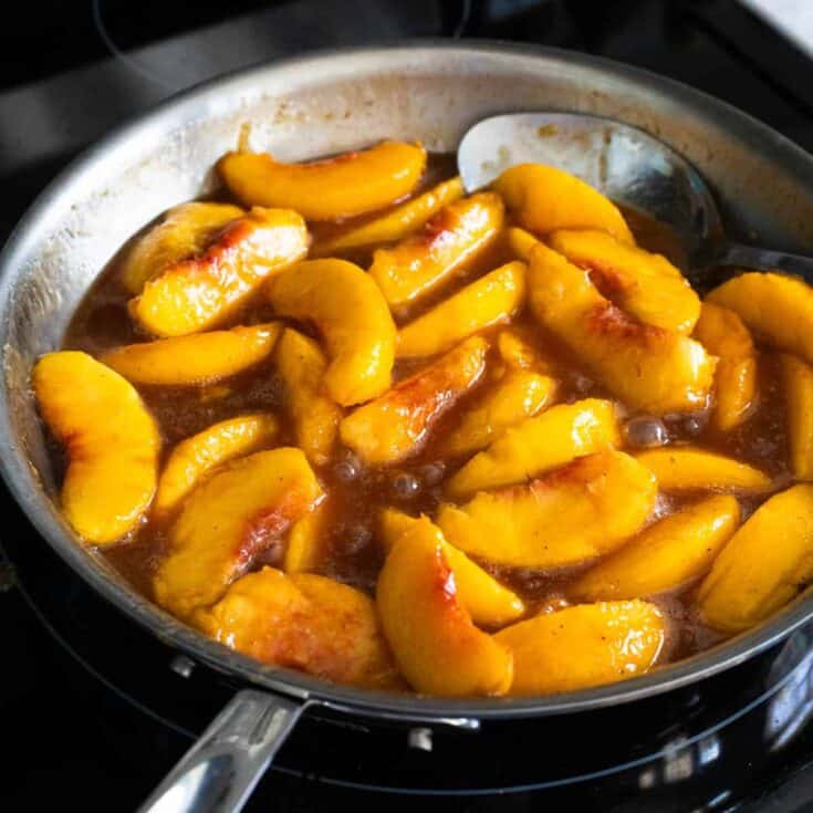 A skillet filled with fried peaches in a butter and brown sugar sauce.