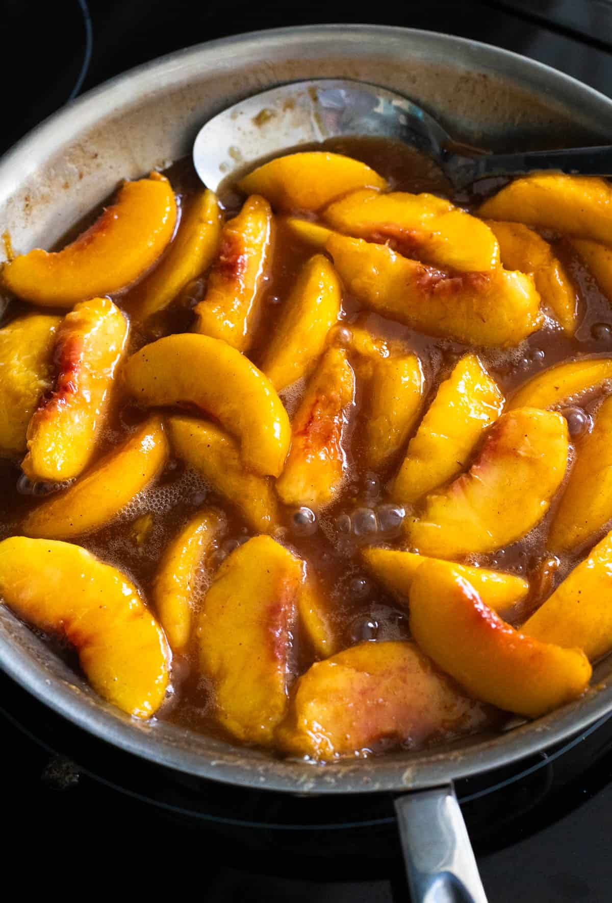 Peach slices simmering in a bubbling caramel sauce in a skillet, being cooked for skillet fried peaches.