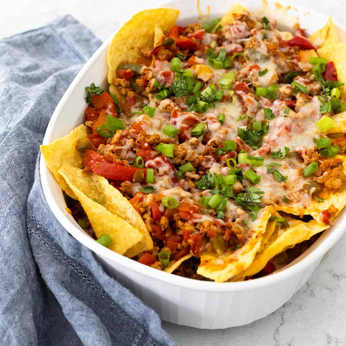 A casserole made with layers of nacho chips, turkey chorizo, vegetables, and melted cheese is cooling.