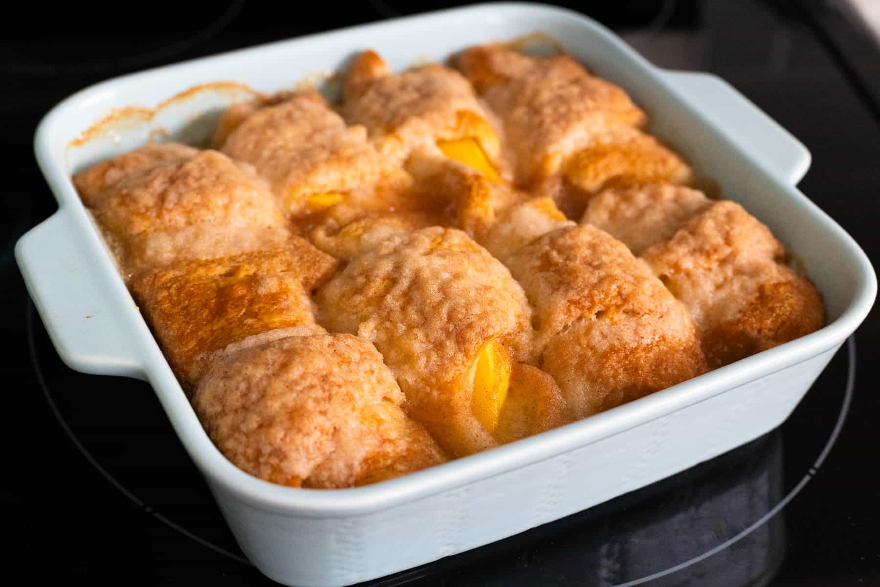 The baking pan filled with golden brown dumplings is cooling on the stovetop.