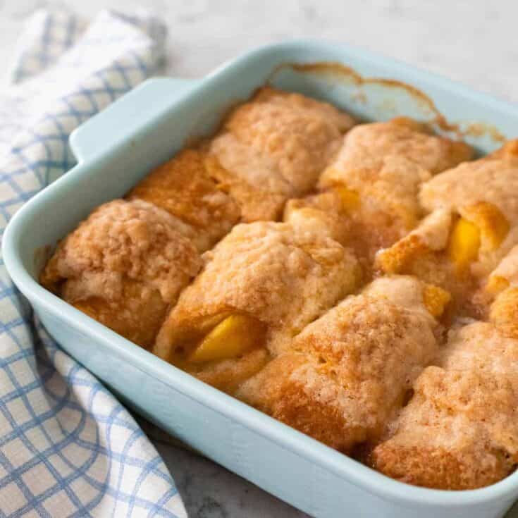 A blue baking dish is filled with warm peach dumplings wrapped in crescent rolls.