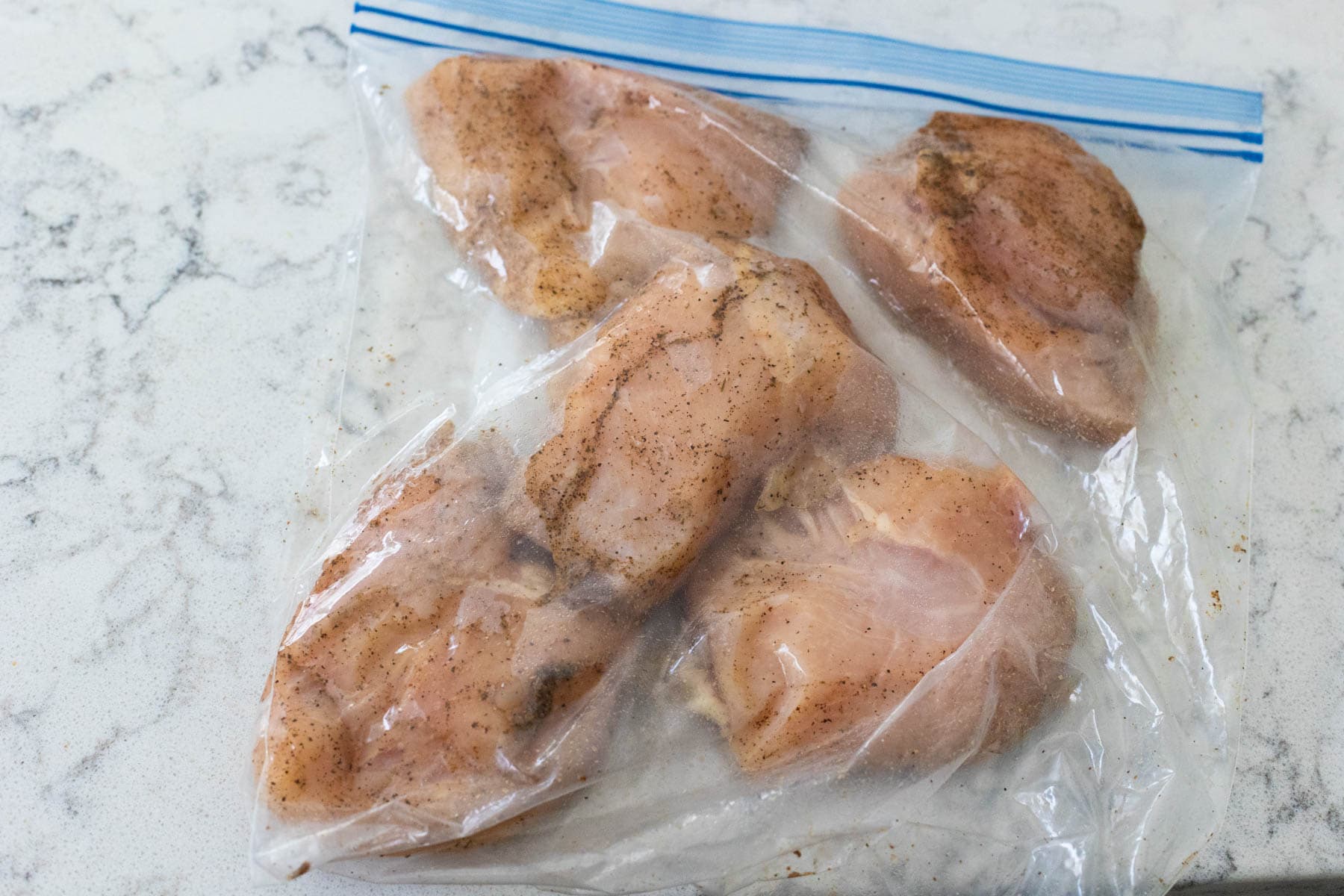 Prepping the raw seasoned chicken to pound inside a large ziptop bag.