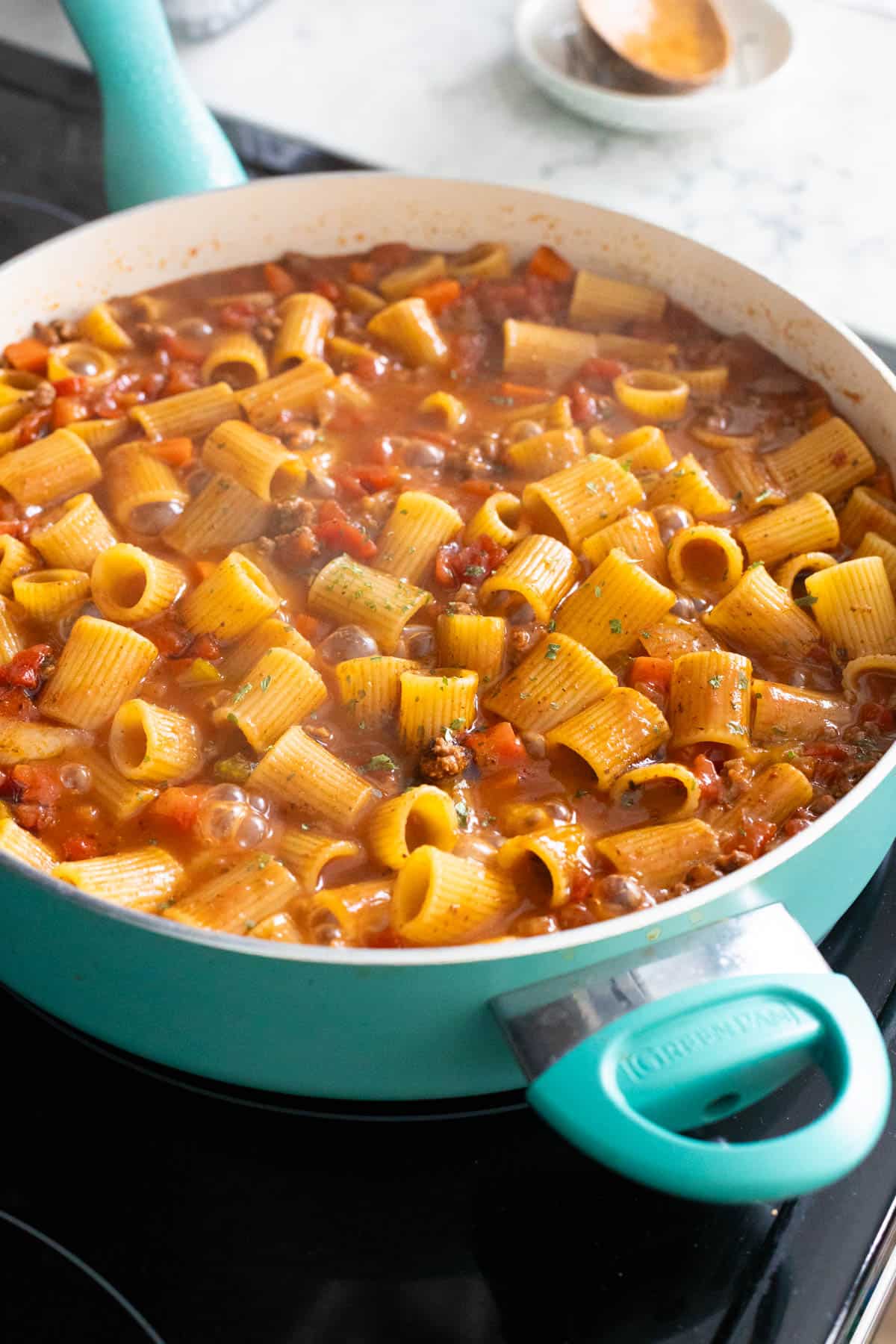 Rigatoni pasta simmering in a rich beef and tomato sauce in a large teal pan.