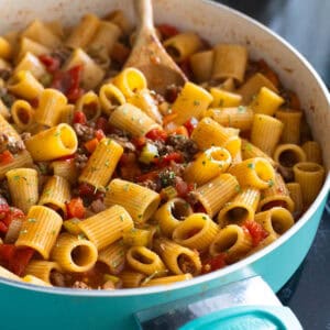 A blue skillet is filled with rigatoni and ground beef in a tomato sauce.