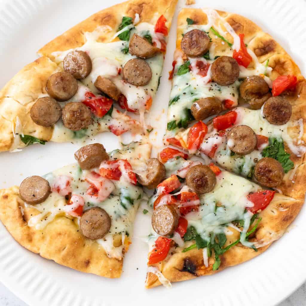A sliced personal-sized breakfast pizza topped with sliced breakfast sausage is on a plate.