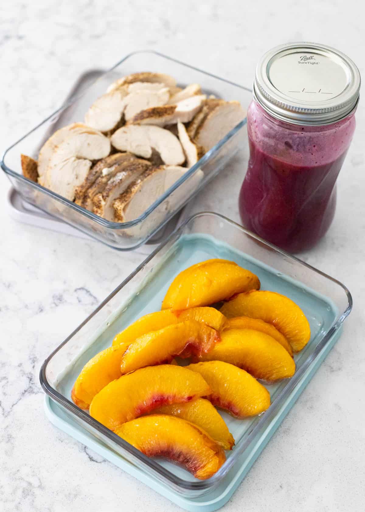 Sliced cooked chicken, roasted peaches, and a jar of blueberry vinaigrette ready for a Chicken Peach Salad.