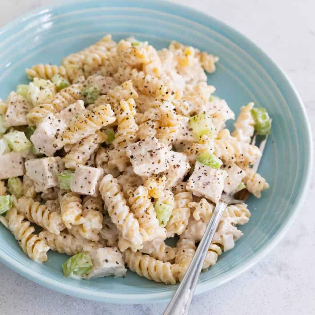 A blue bowl is filled with creamy pasta salad with chunks of chicken and chopped celery.