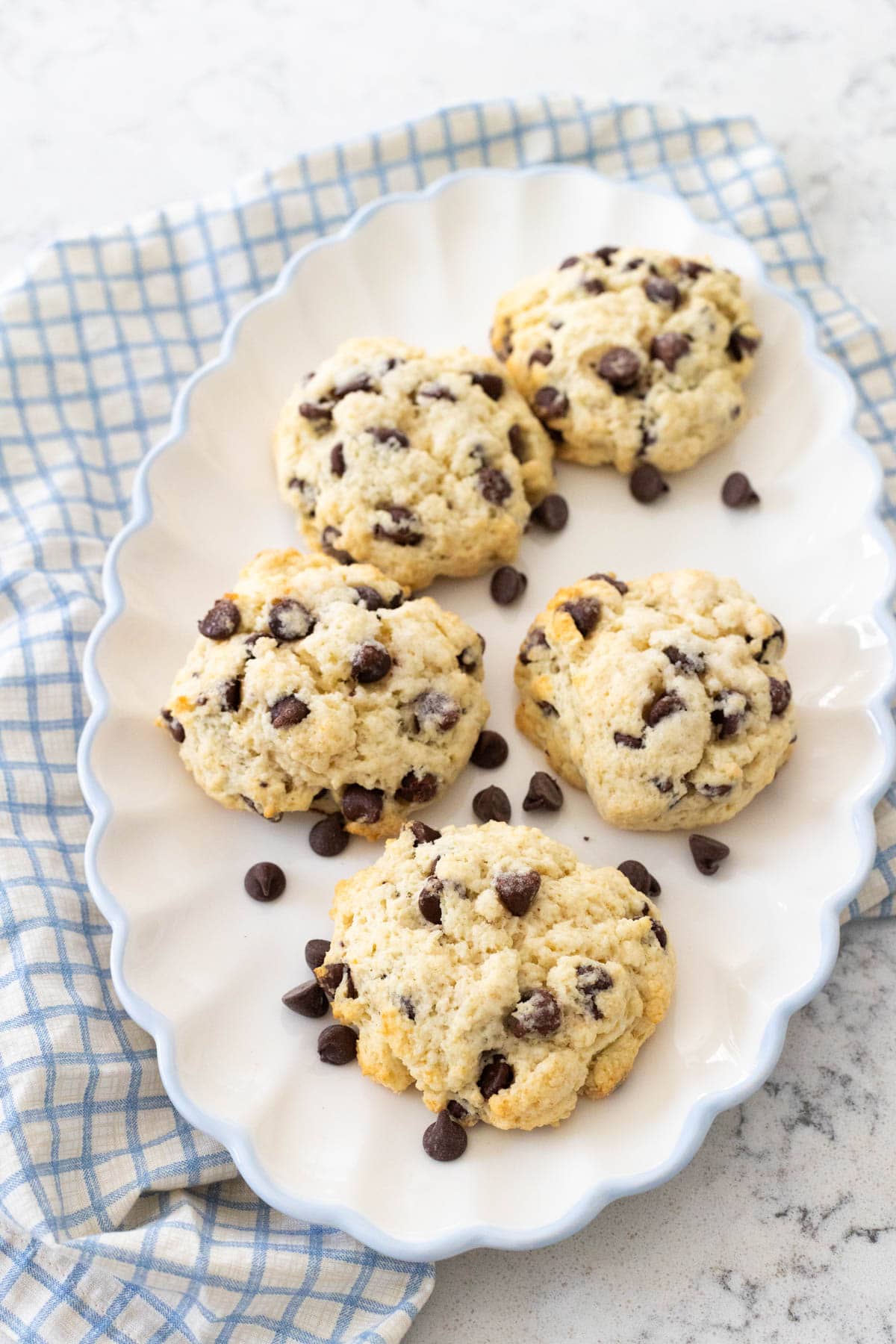 Freshly baked chocolate chip scones on a white scalloped plate, with a few chocolate chips scattered around.