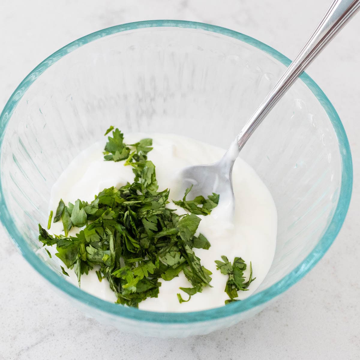 Bowl of sour cream topped with chopped fresh cilantro and a spoon inside.