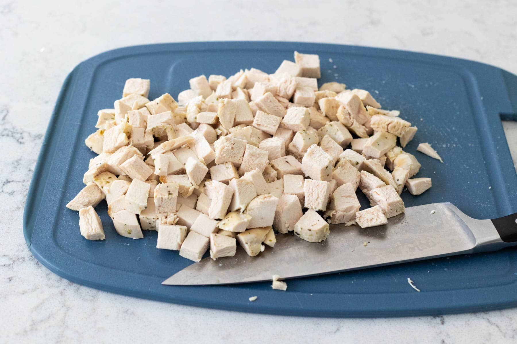 A cubed cooked chicken breast on a blue cutting board with a knife beside it.