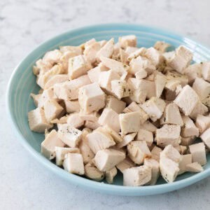 A blue bowl is filled with perfectly sliced cubed chicken ready for sprinkling over a salad.