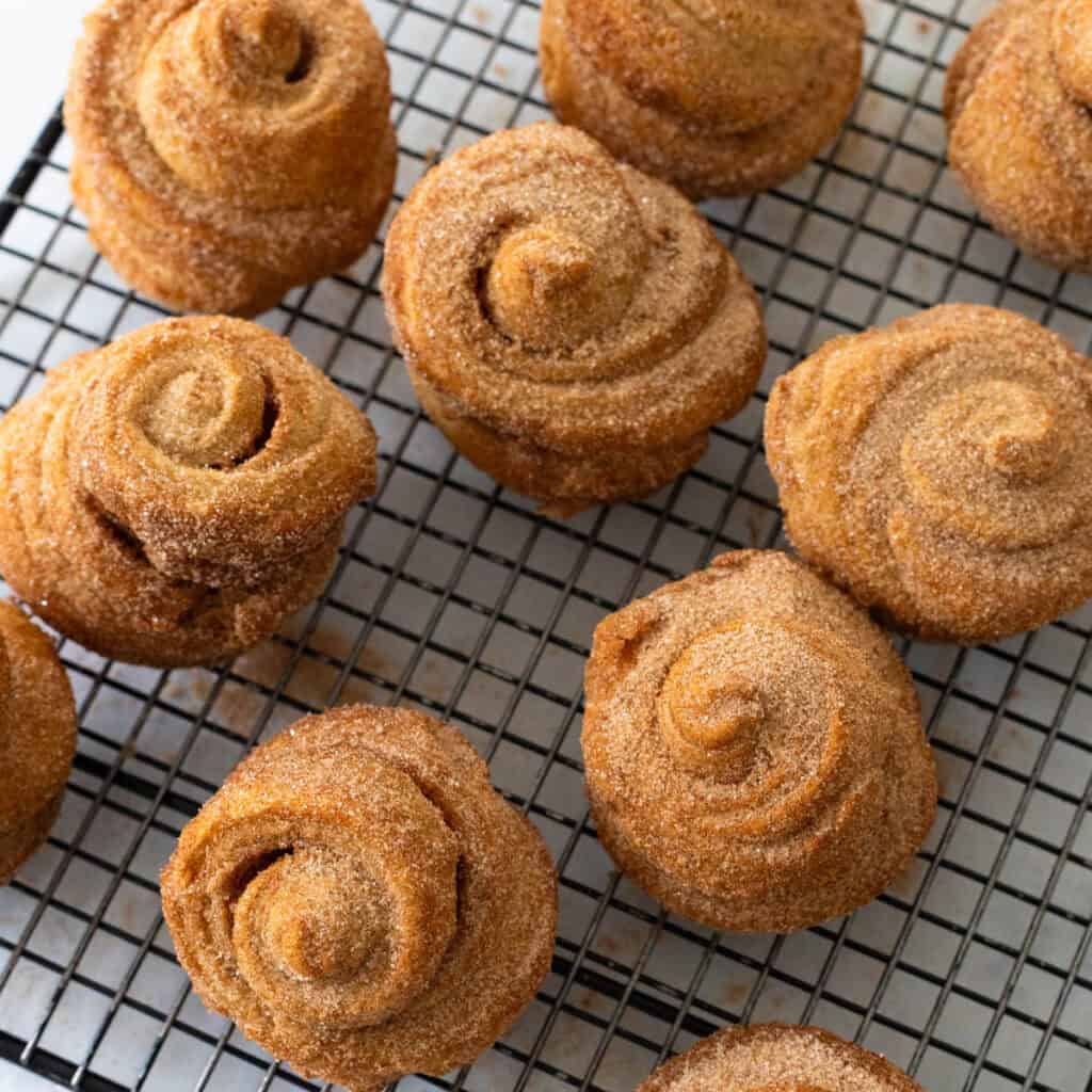 Cinnamon sugar coated puff pastry swirls are cooling on a wire rack.