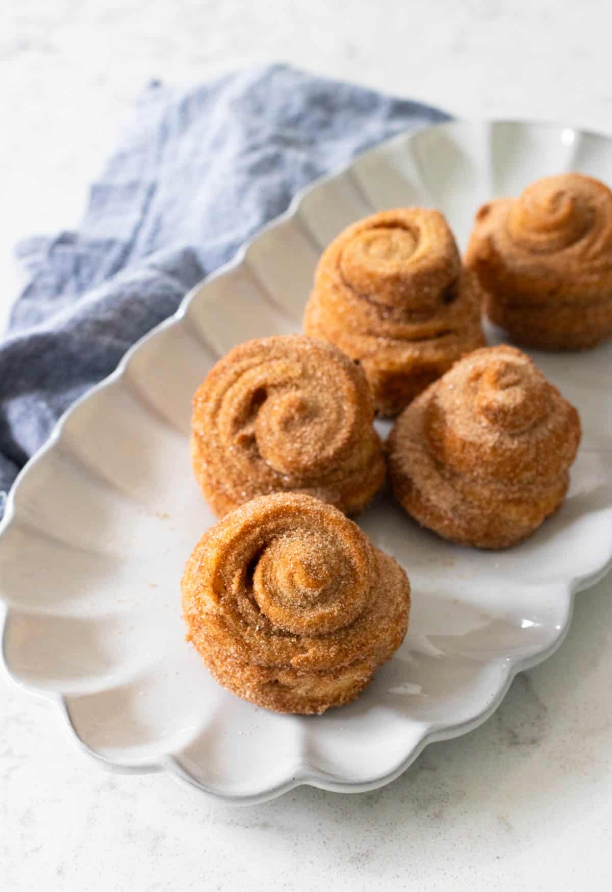 Freshly baked cinnamon sugar cruffins arranged on a white serving plate, highlighting their swirled layers and golden, sugary coating.