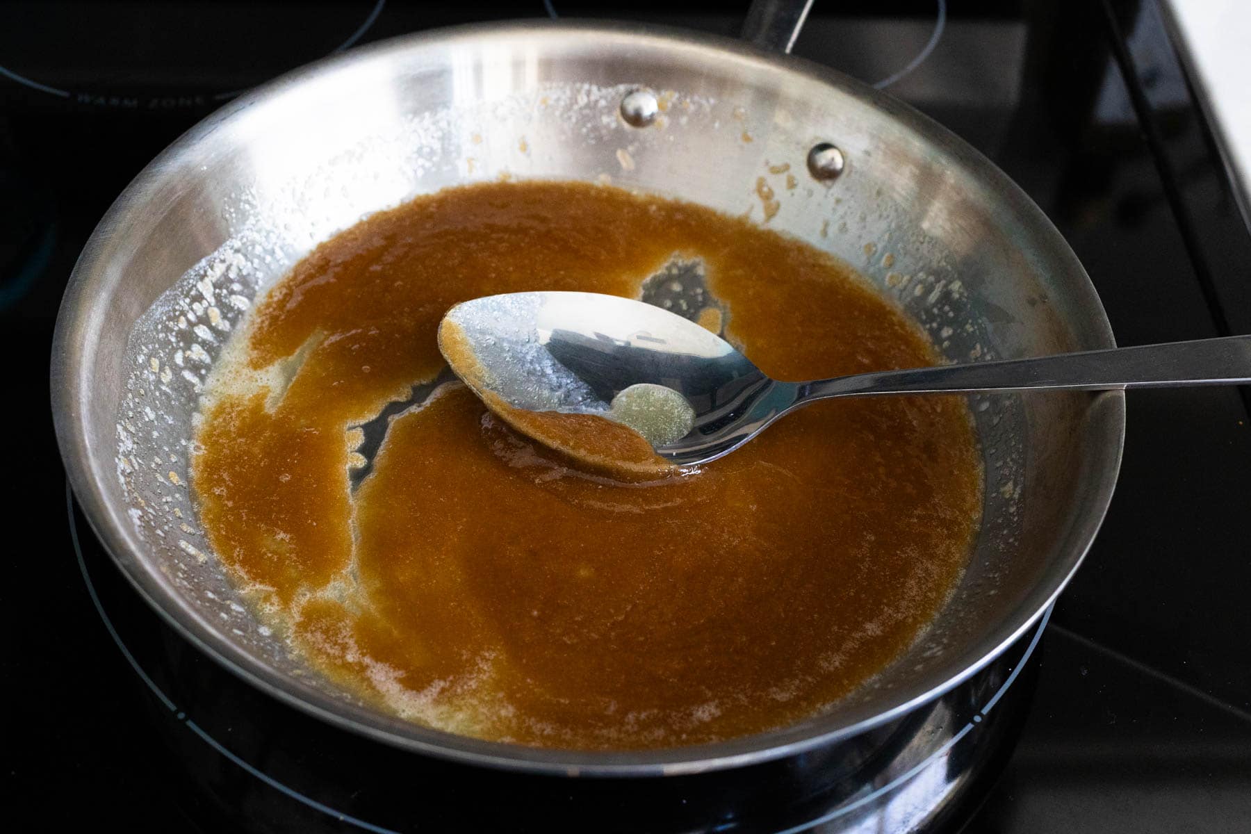 Spoon stirring melted butter and brown sugar mixture in a skillet on the stove, forming the caramel base for skillet fried peaches.