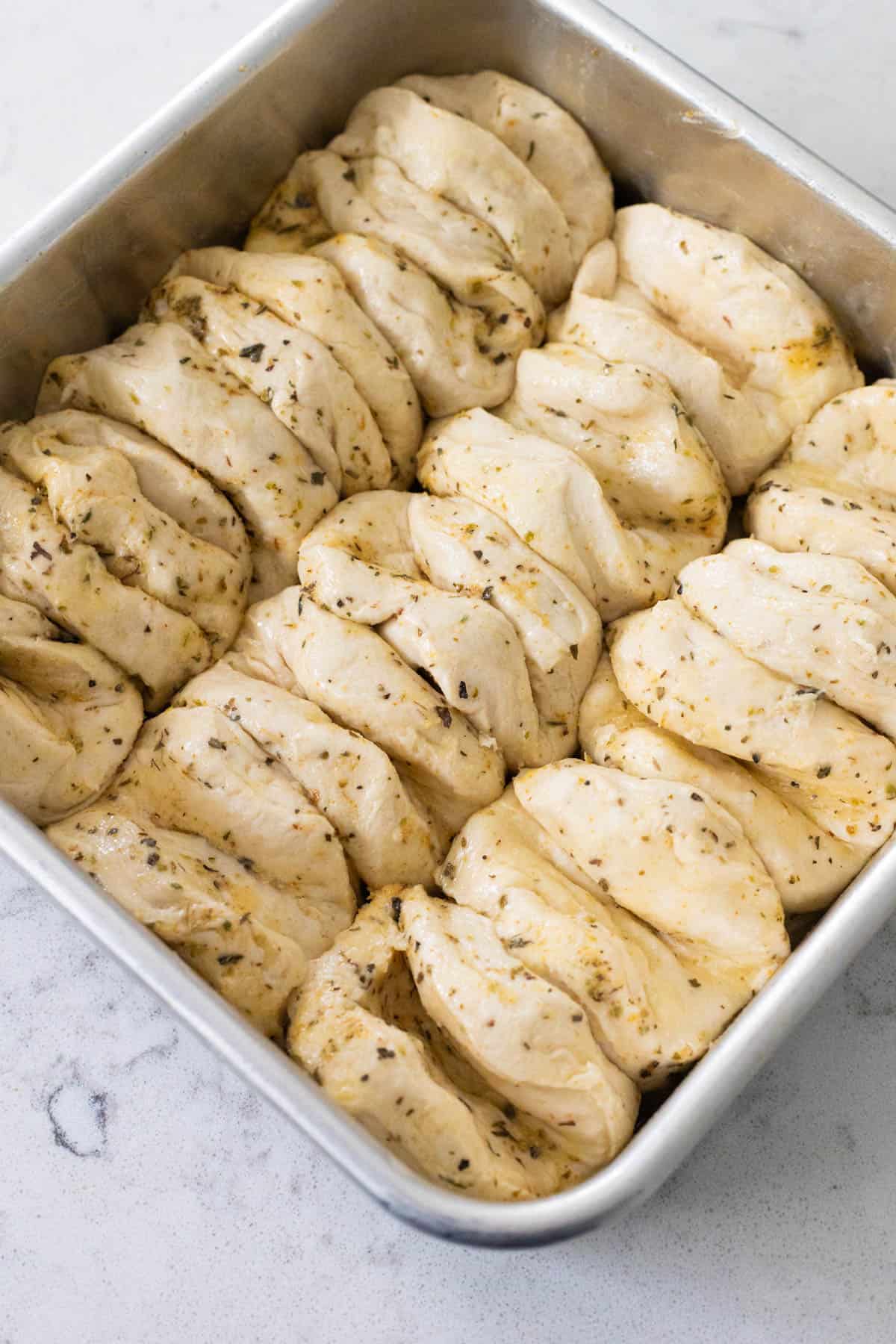 Unbaked herb butter biscuits layered and arranged in a metal baking pan.