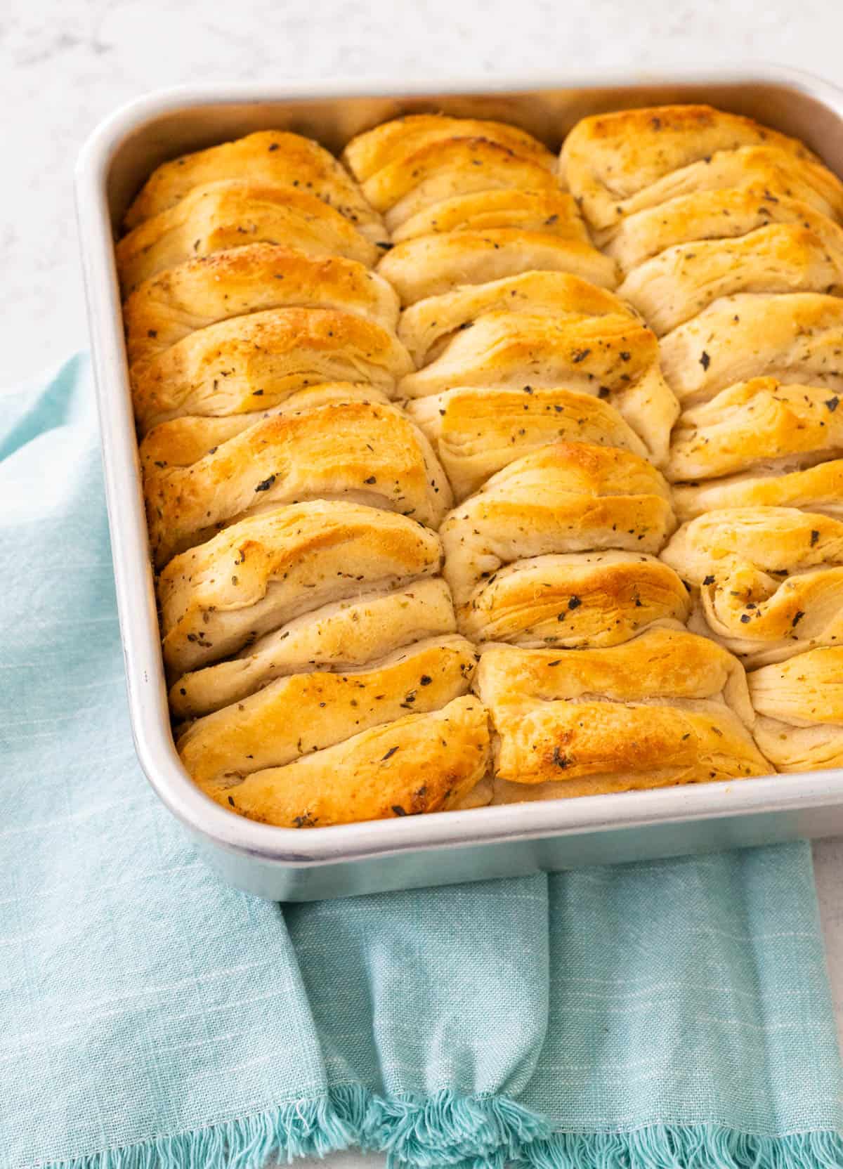 Stacked herb butter biscuits baked to golden brown in a metal pan.