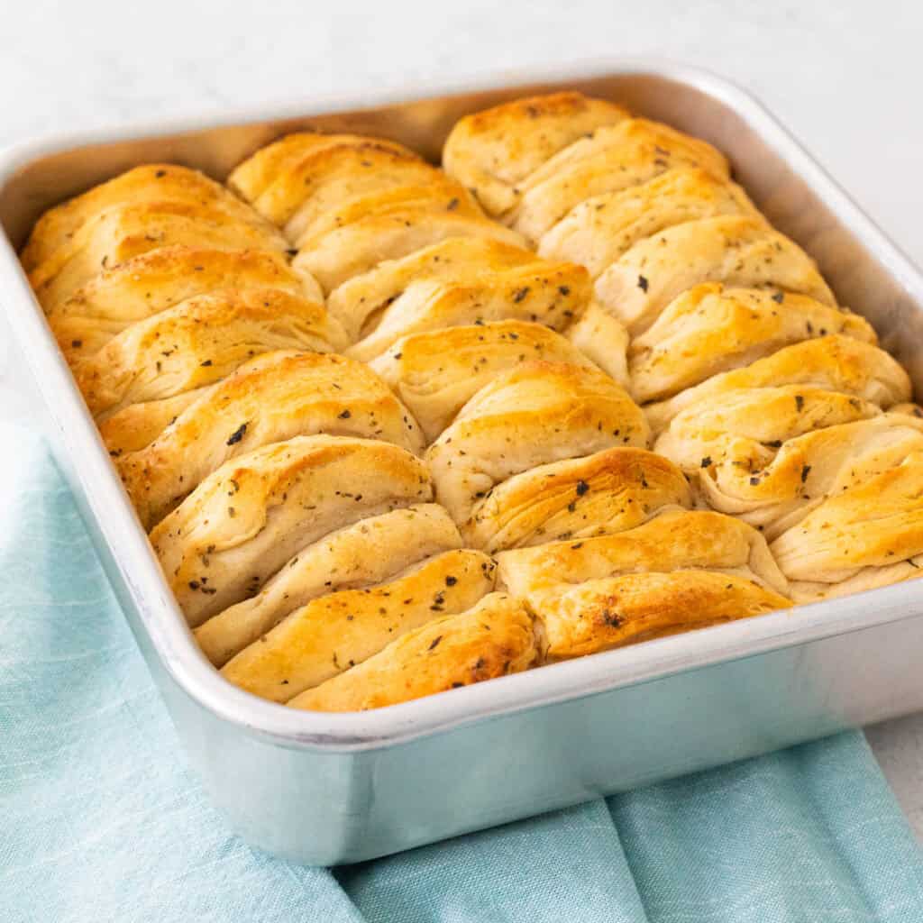 A square metal baking pan is filled with golden brown buttery biscuits.