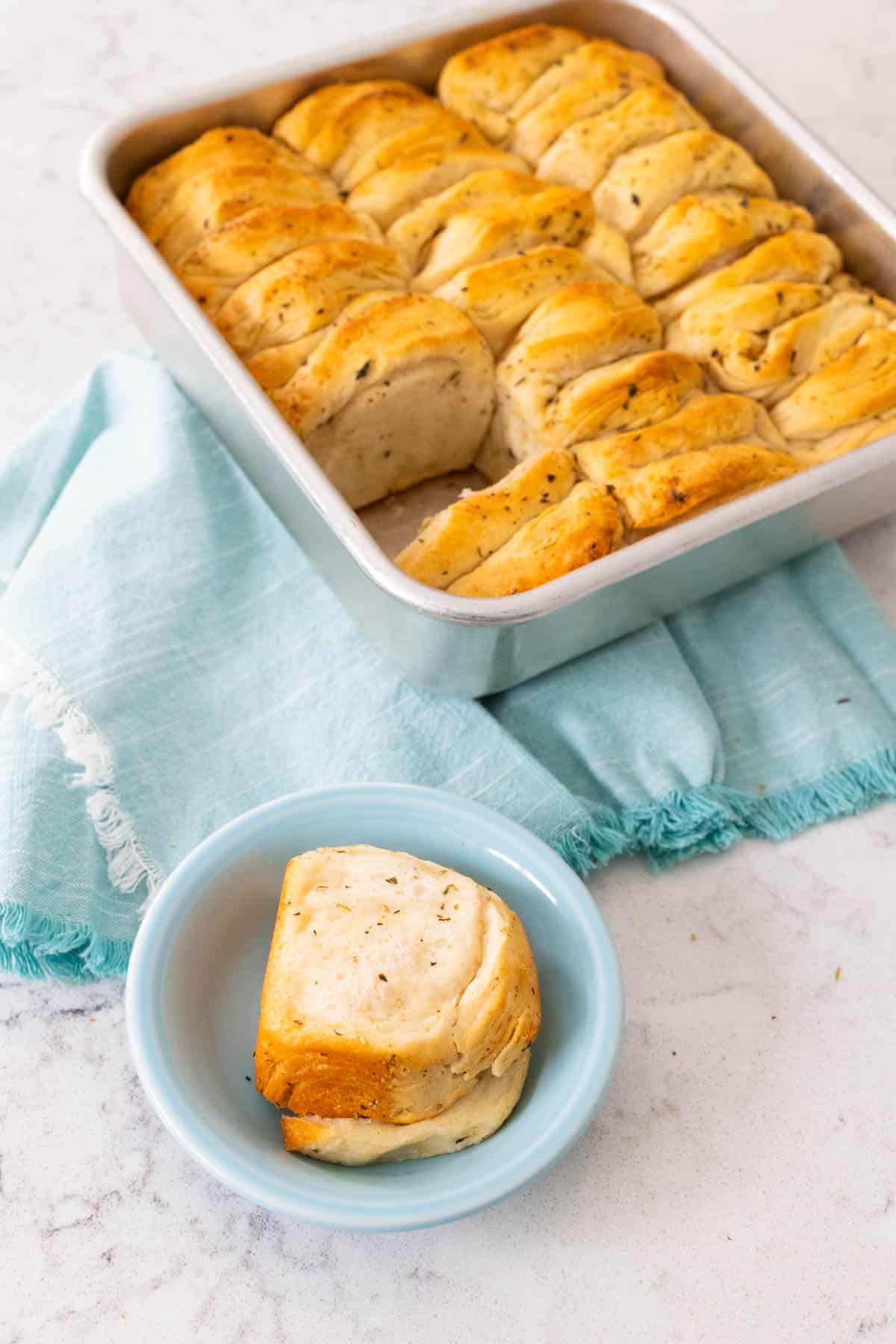 Freshly baked herb butter biscuits in a baking pan with one served on a small blue dish.