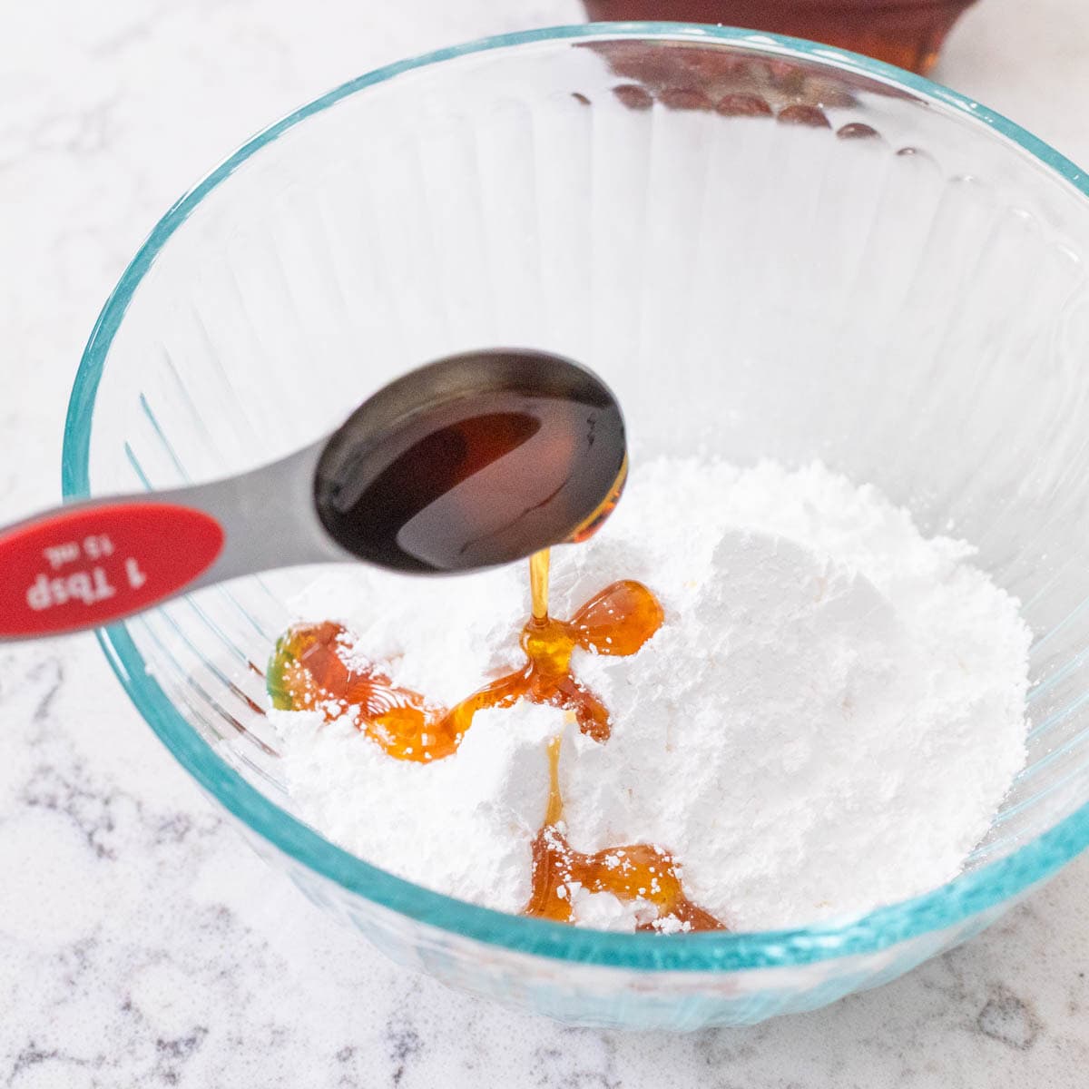 Vanilla extract being poured into powdered sugar in a glass bowl to make maple glaze.