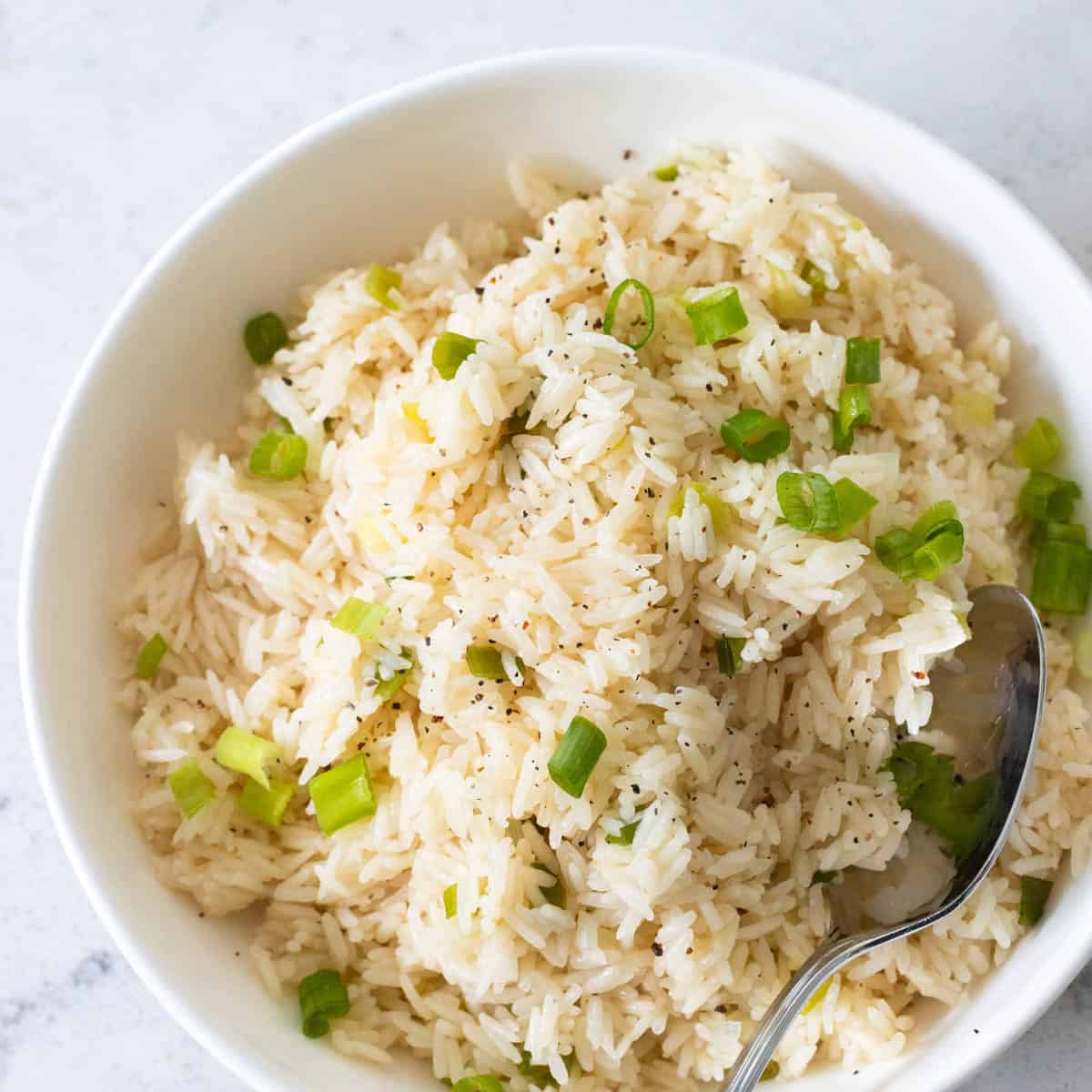 A white bowl filled with white rice mixed with green scallions.
