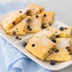 A white platter is filled with square-shaped pancakes that have been baked on a sheet pan and then sliced and served for a crowd.