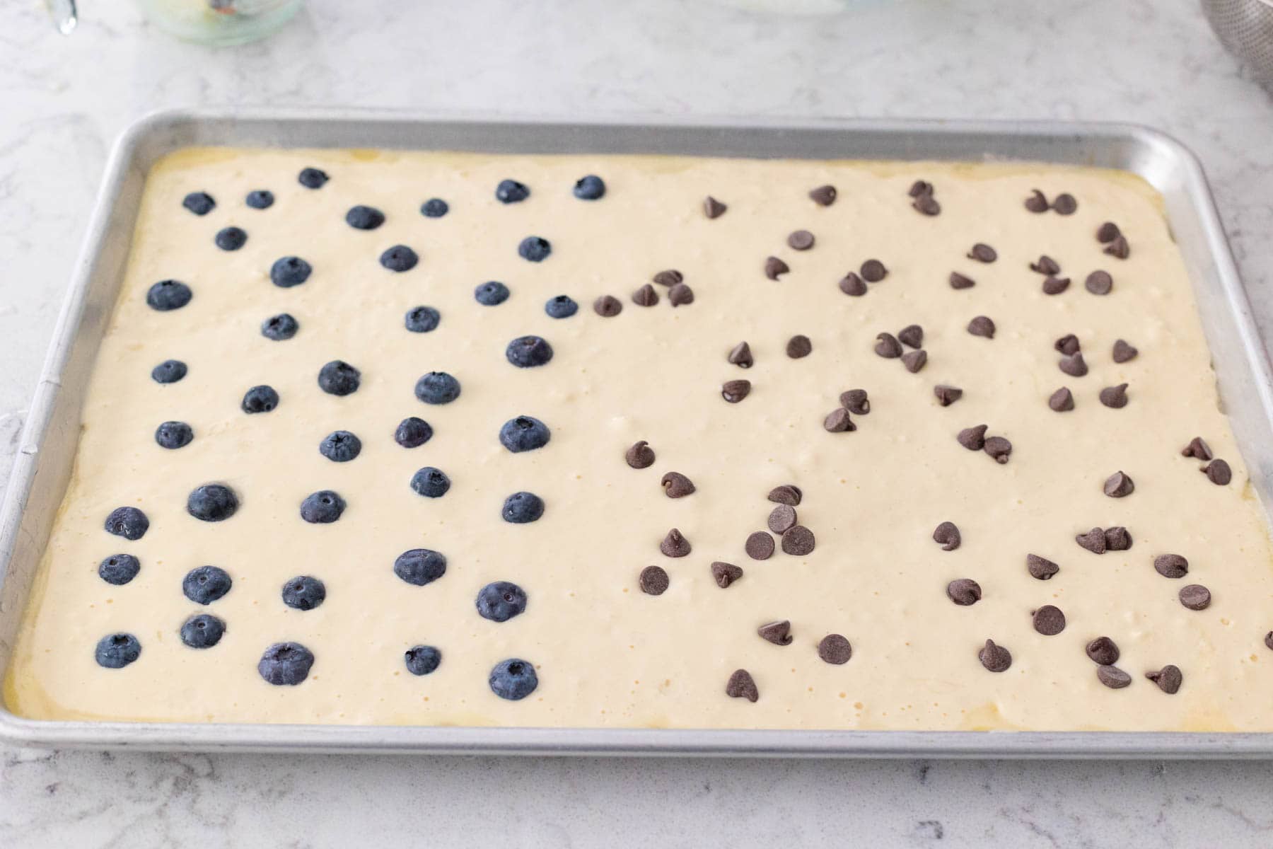 The blueberries and chocolate chips have been scattered across the surface of the sheet pan pancake batter.