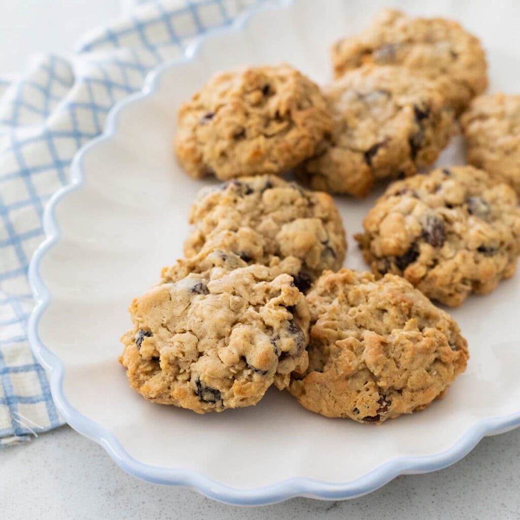A white ruffled platter has a pile of soft oatmeal raisin cookies ready to be served.