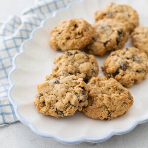 A white ruffled platter has a pile of soft oatmeal raisin cookies ready to be served.