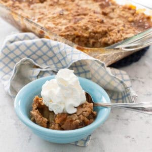 A small blue bowl is filled with some apple dump cake and topped with whipped cream.