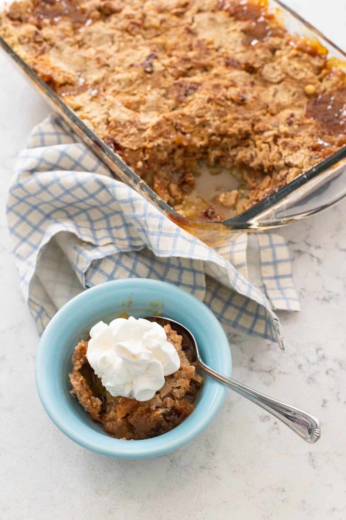 A small blue bowl is filled with some apple dump cake and topped with whipped cream.