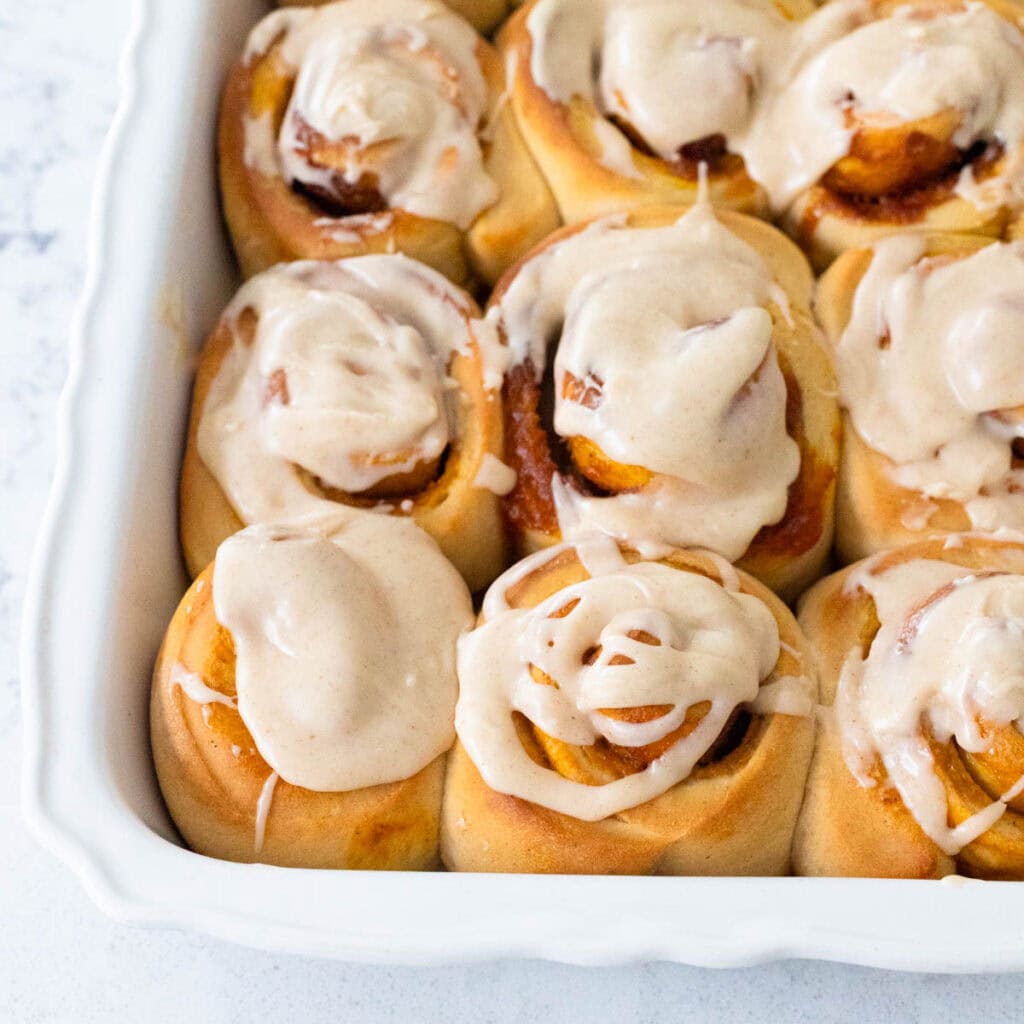 A pan of cinnamon rolls has browned butter glaze drizzled over the top.