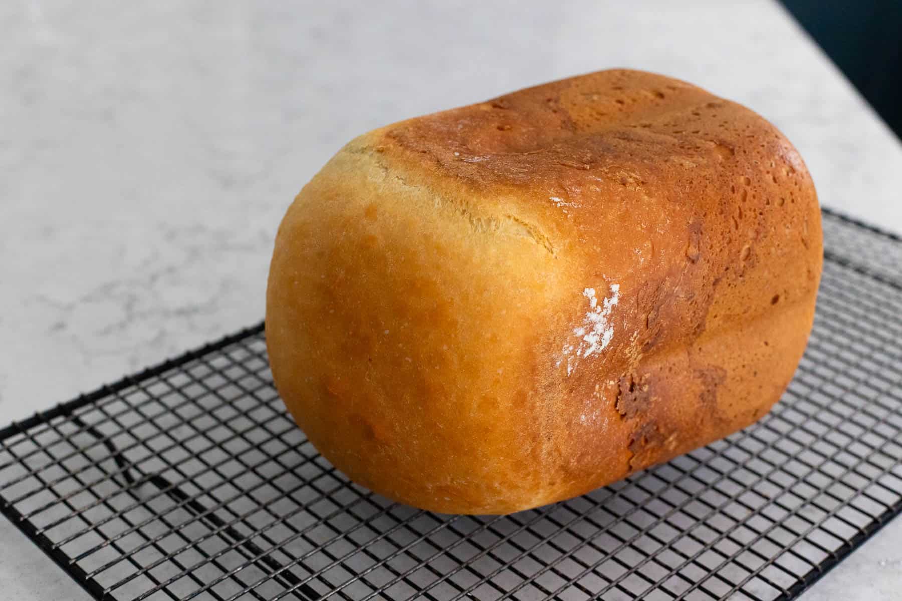 The photo shows a golden loaf of cottage cheese bread resting on a wire cooling rack after baking.