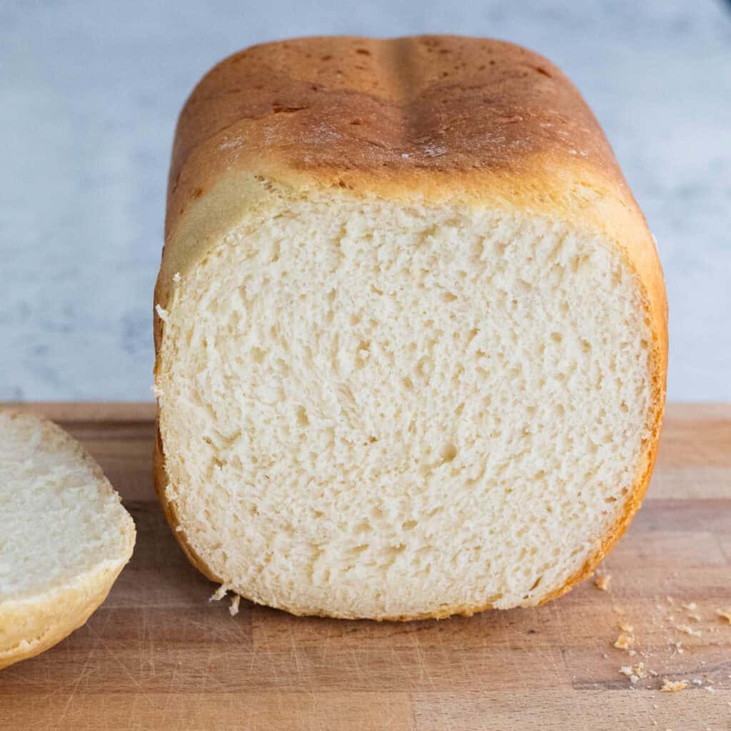 The loaf of bread machine bread has been sliced to show the light and fluffy interior of bread.