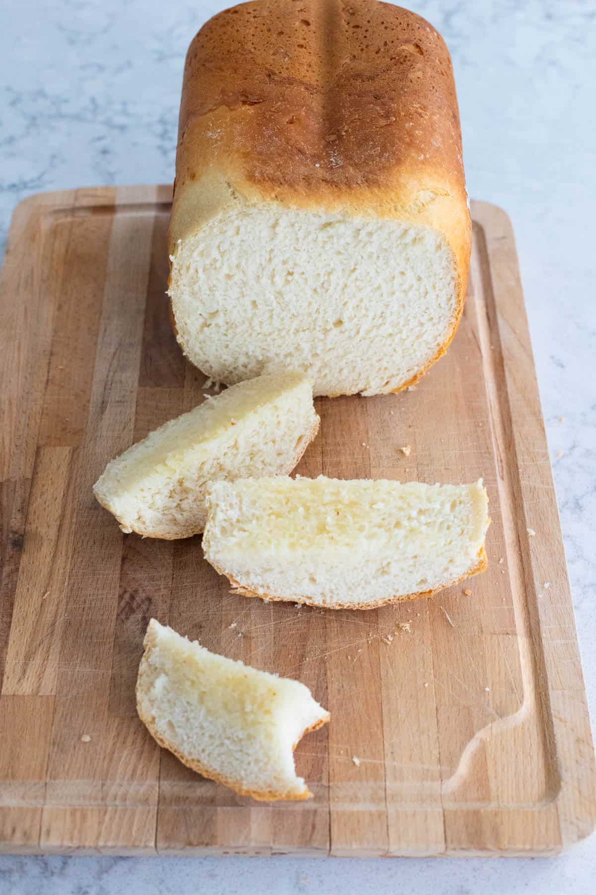A loaf of cottage cheese bread on a wooden cutting board with several soft, thick slices cut from the end.