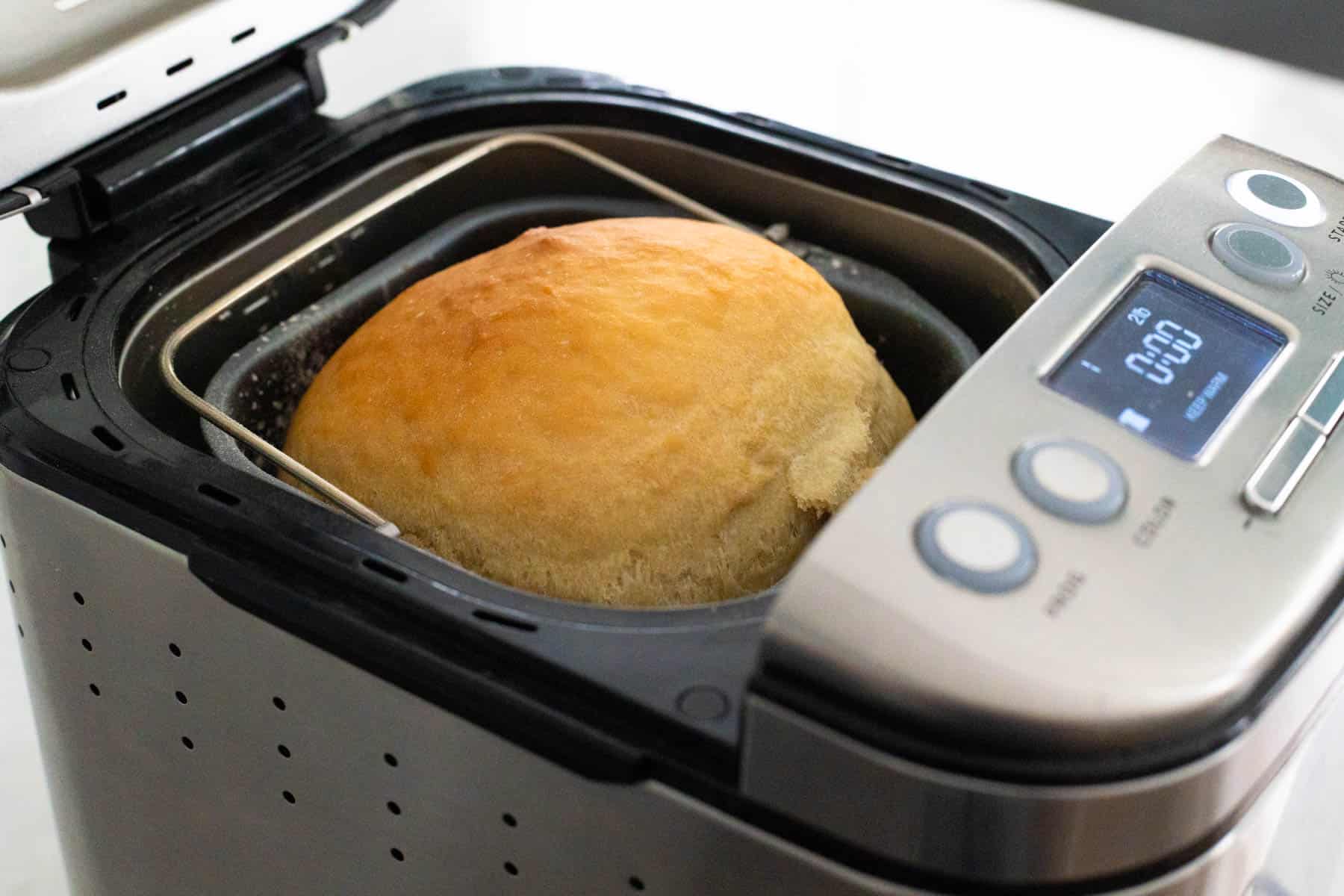 The photo shows a freshly baked golden loaf of cottage cheese bread still in the bread machine pan with the lid open.