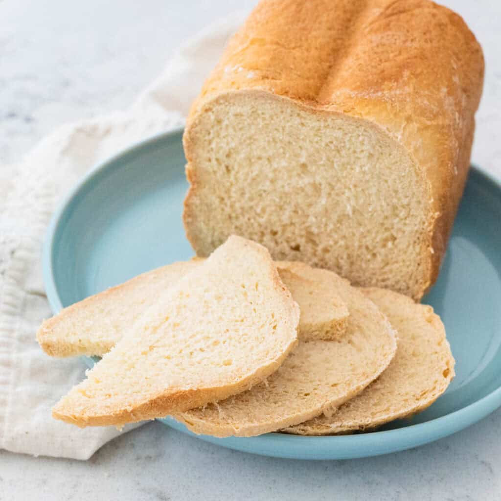 A loaf of bread machine French pear bread has been sliced and served on a blue plate.