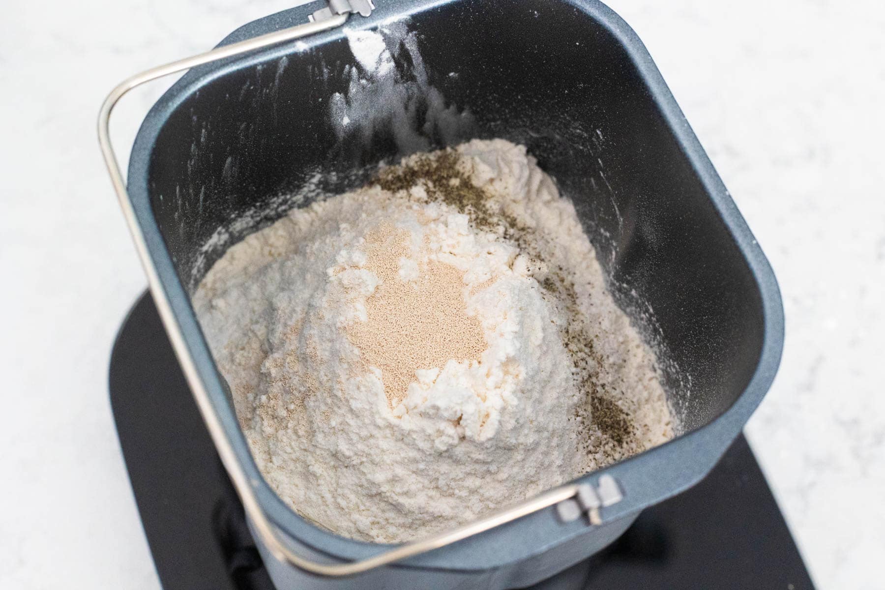 Flour, yeast, and spices layered on top of the mashed pear mixture inside the bread machine pan before mixing.